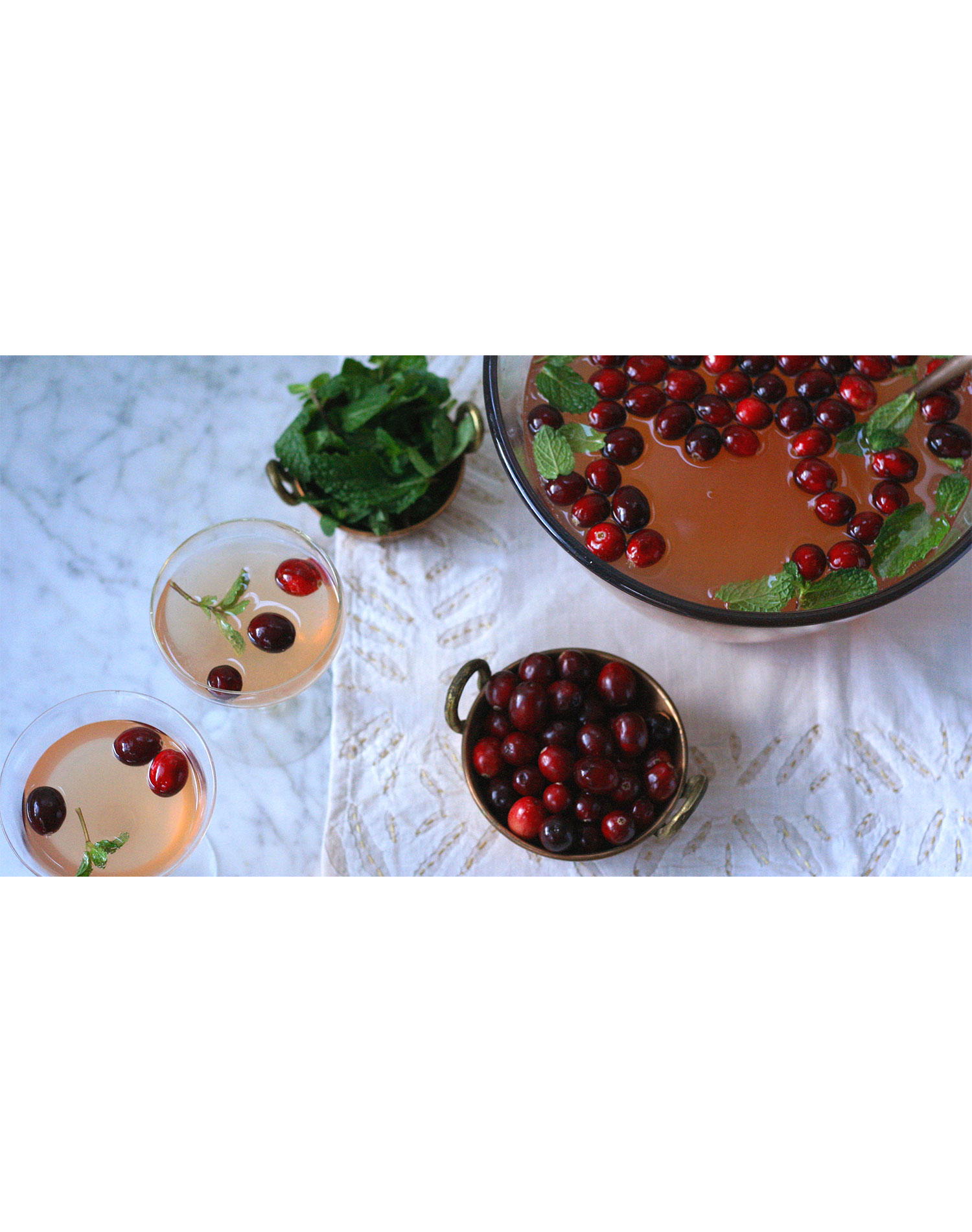 holiday punch bowl cocktails: cranberry mint cocktail in a bowl with two glasses and a bowl of cranberries