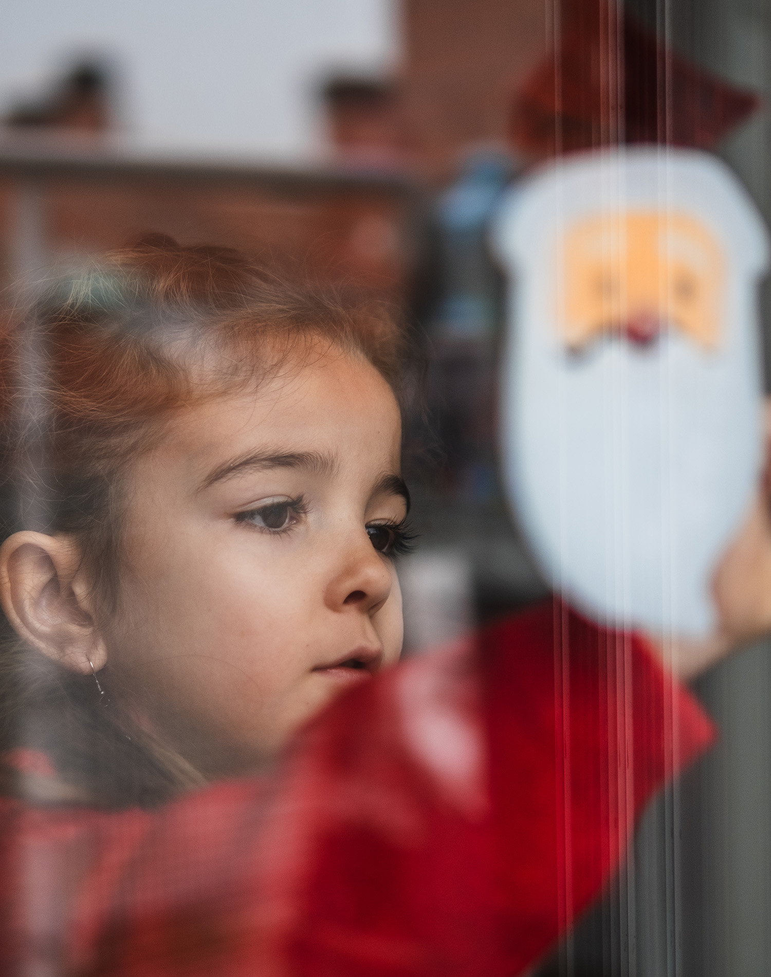 Little girl looks through Christmas decorated window